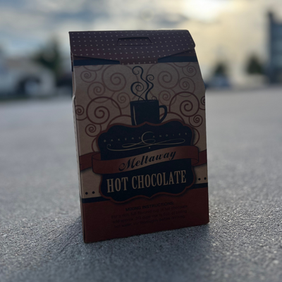Baker's Candies 14oz Meltaway Hot Chocolate product pictured on concrete with a blurred background.