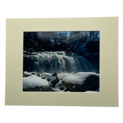 Photograph Of A Waterfall Behind Large, Snow-Covered Rocks With A Cream Colored Border