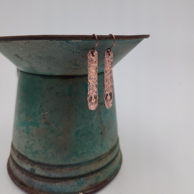 Bar Shaped Dangle Copper Earrings With Hand Stamped Horseshoe Design Dangling from Blue Vase