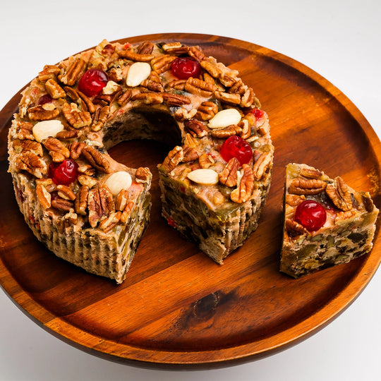 Wooden plate with a fruitcake dessert and a slice removed, on a white background