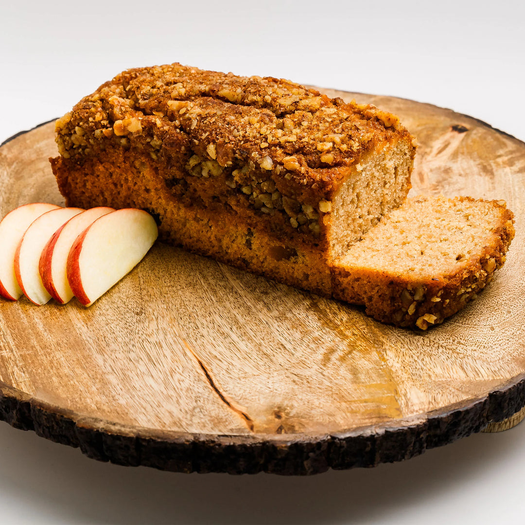 Loaf of bread with a slice cut, accompanied by apple slices on a wooden board.