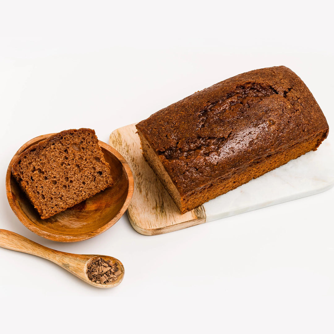 Loaf of chocolate merlot bread with a slice on a wooden plate, on a white background