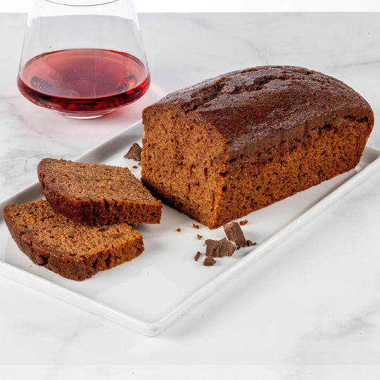 Chocolate merlot loaf cake with two slices on a white plate, accompanied by a glass of red wine.