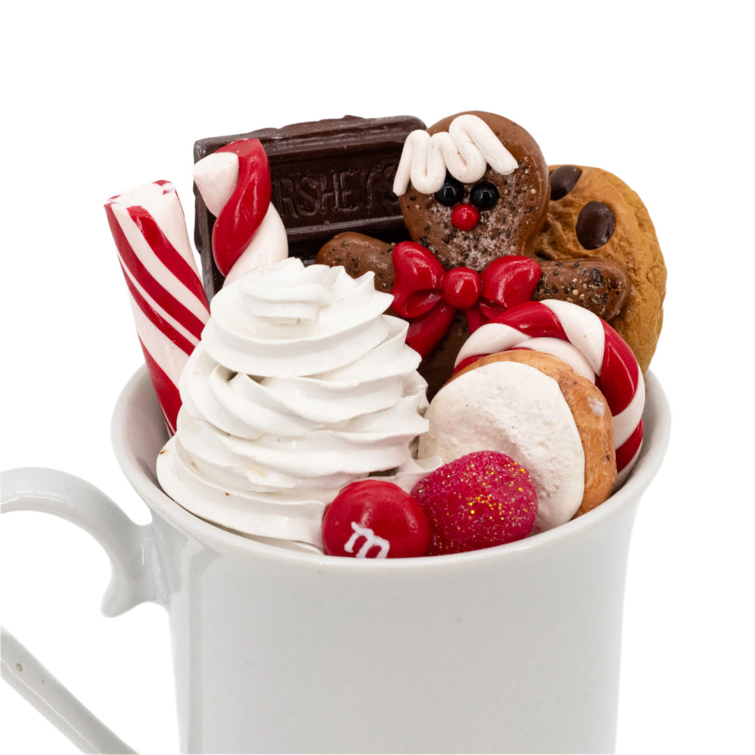 Hot chocolate with whipped cream, candy, and gingerbread man decoration in a white mug.