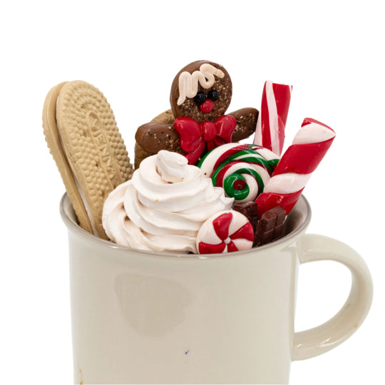 Mug filled with whipped cream, cookies, and candy canes on a white background