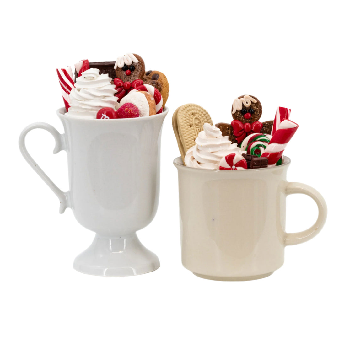 Two mugs filled with whipped cream, cookies, and candy on a white background