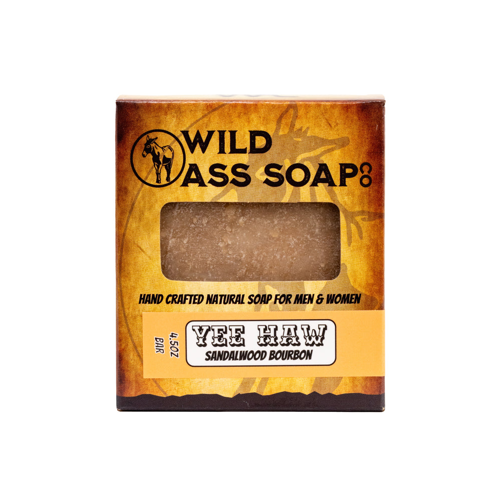 A bar of soap with a brownish tint, packaged in a rectangular box with a logo and the text 'WILD ASS SOAP’S YEE HAW Sandalwood Bourbon'.