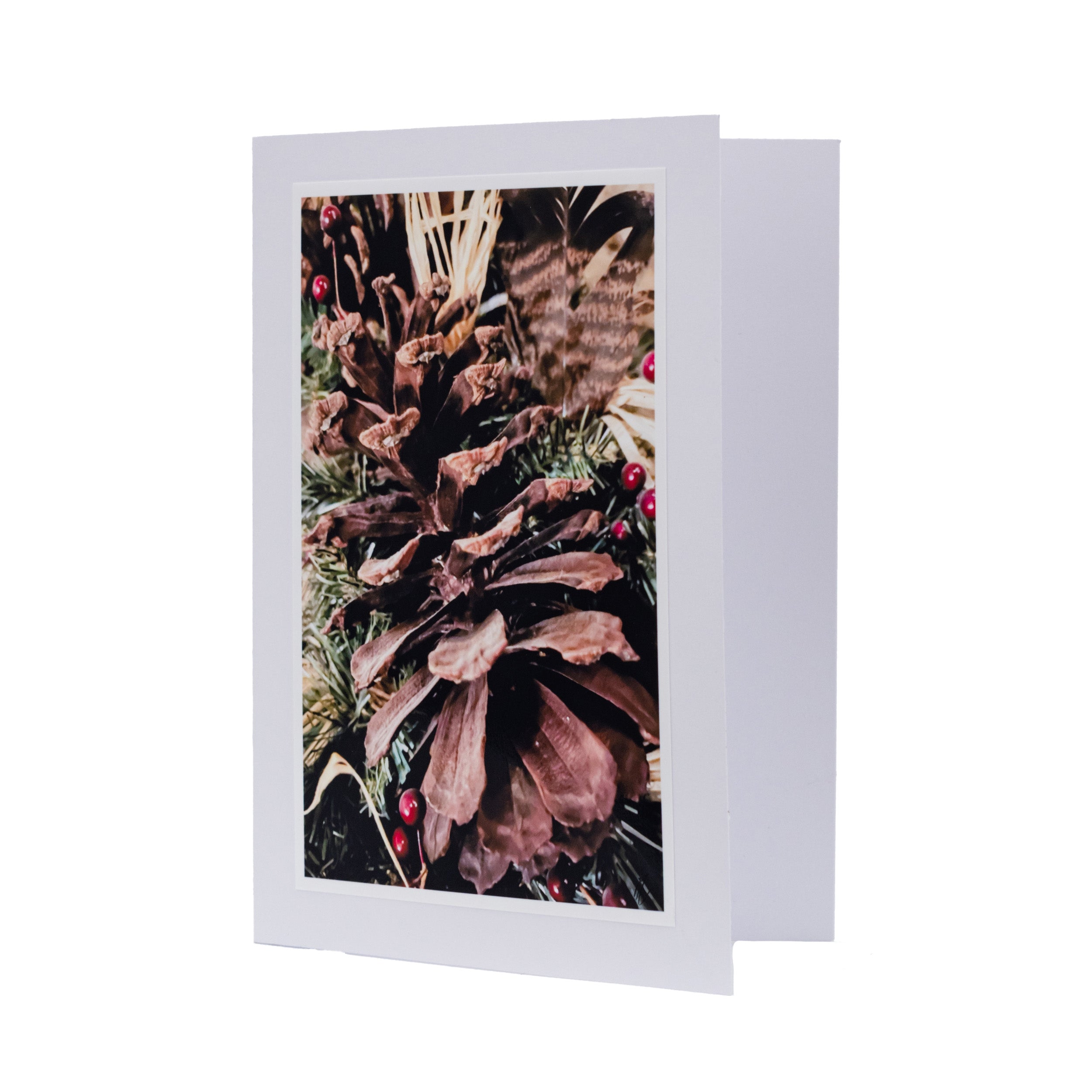 A Christmas-themed greeting card with a close-up photo of a pine cone surrounded by pine needles, set against a white background.