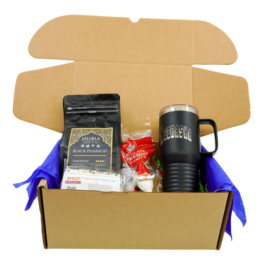 Open cardboard box containing a black tumbler, coffee package, and other items on a white background