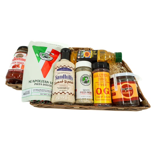 Basket of Nebraska products including sauce, dough, honey, oil, salad dressing and seasonings on a white background