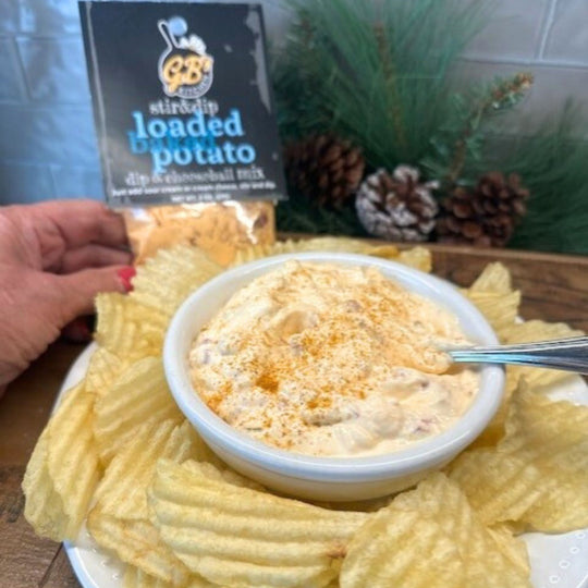 Bowl of loaded potato dip with chips and a package of dip mix in the background.