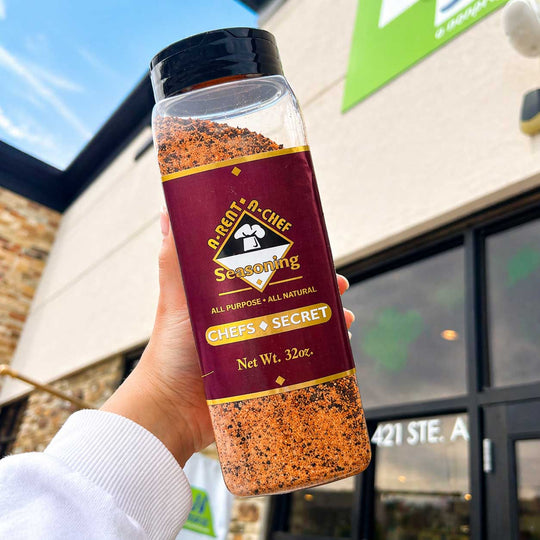 Hand holding a bottle of A-Rent-A-Chef  seasoning with a store exterior in the background.