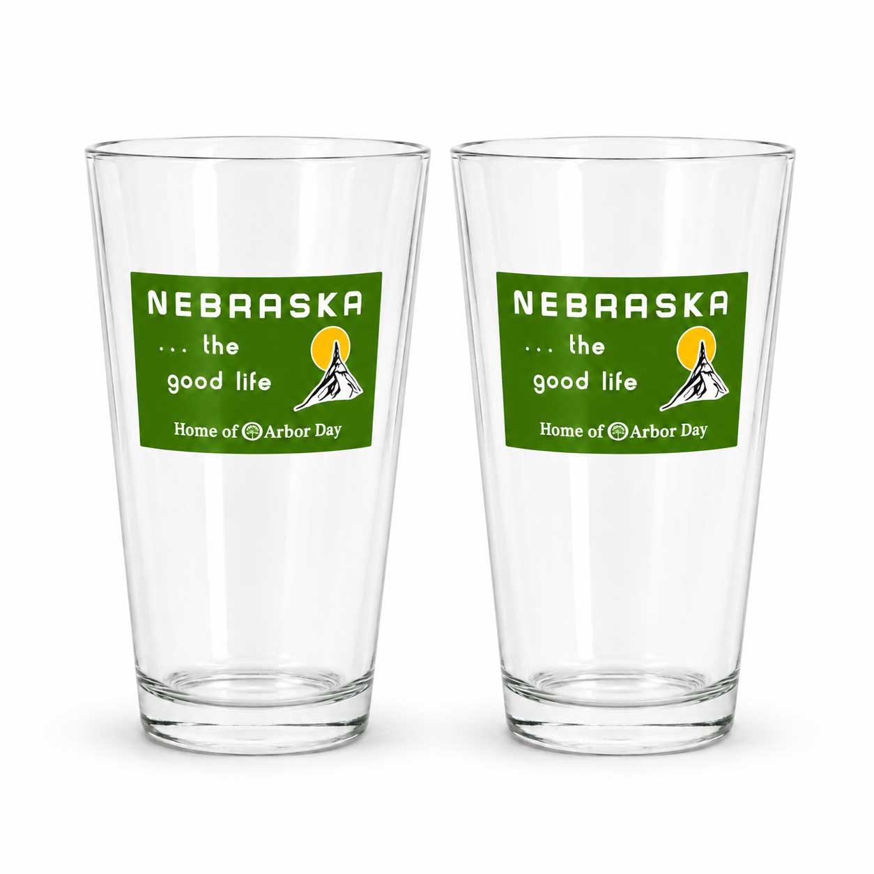 Two clear pint glasses with a green Nebraska graphic on the front, displayed side by side on a white background.
