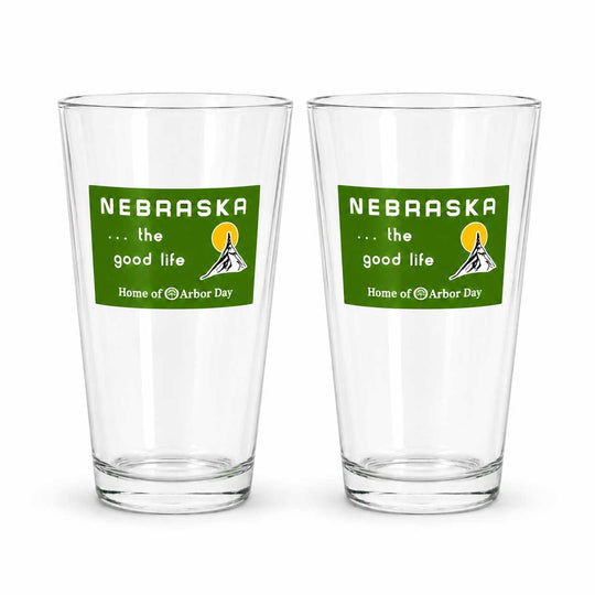 Two clear pint glasses with a green Nebraska graphic on the front, displayed side by side on a white background.