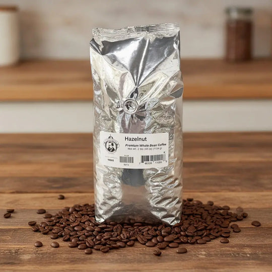 Silver package of hazelnut coffee beans on a wooden surface with scattered beans.