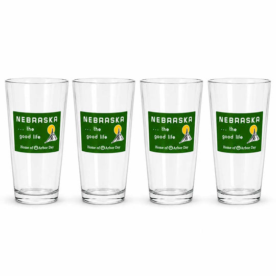 Four clear drinking glasses arranged in a row on a white background, each printed with a green Nebraska graphic that reads 'the good life' and 'Home of the Nebraska Cornhuskers.'.