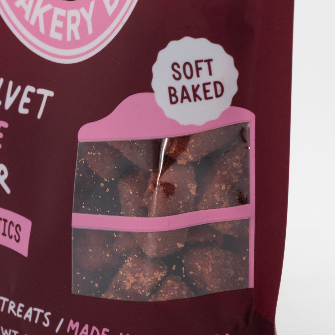Dog treat package with clear window showing treats and 'Soft Baked' label, against a pink and white background.