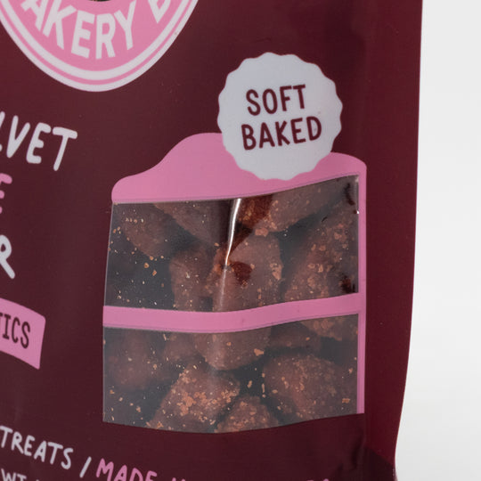 Dog treat package with clear window showing treats and 'Soft Baked' label, against a pink and white background.