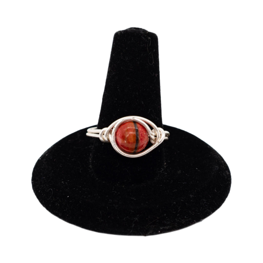 Silver ring with a red stone on a black velvet stand against a white background