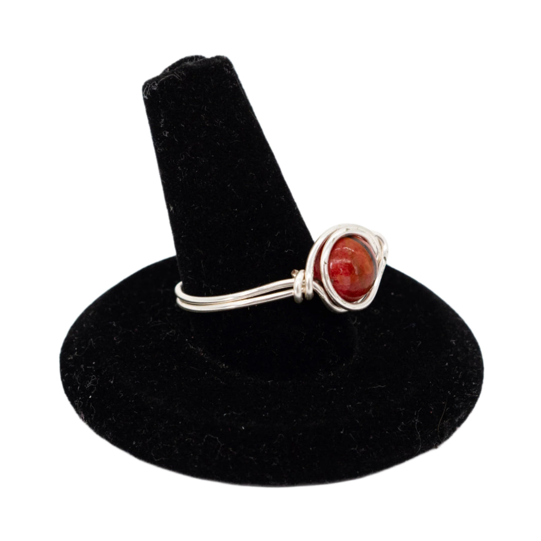 Silver ring with a red stone on a black velvet stand against a white background