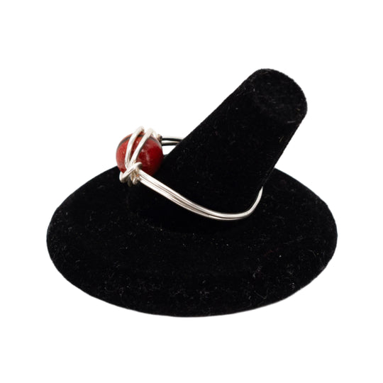 Silver ring with a red stone on a black stand against a white background