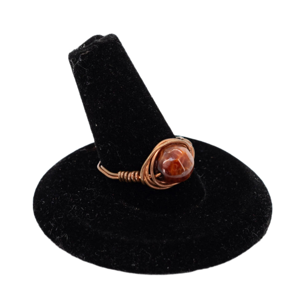 Ring with a brown stone on a black stand against a white background