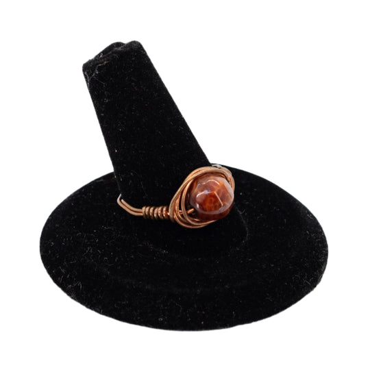 Ring with a brown stone on a black stand against a white background
