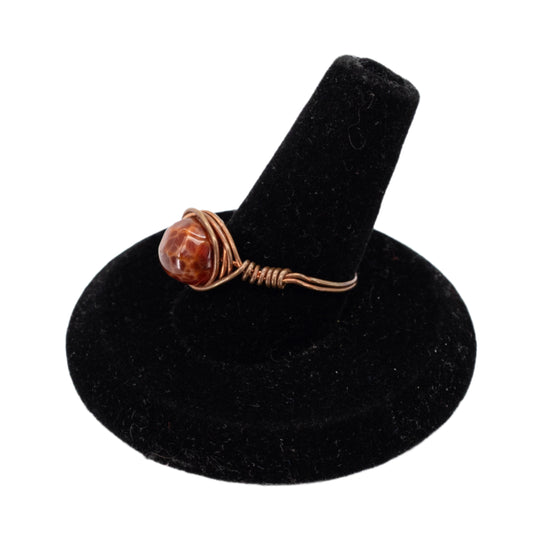 Ring with a brown stone on a black velvet stand against a white background