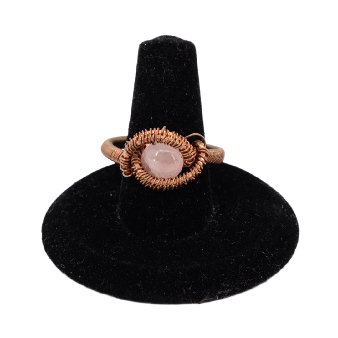 Ring with a pink stone on a black stand against a white background