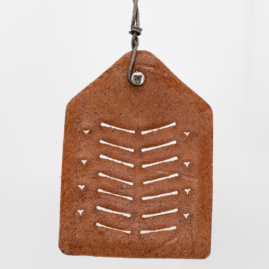 Brown leather tag with white pattern and metal hook on a light gray background