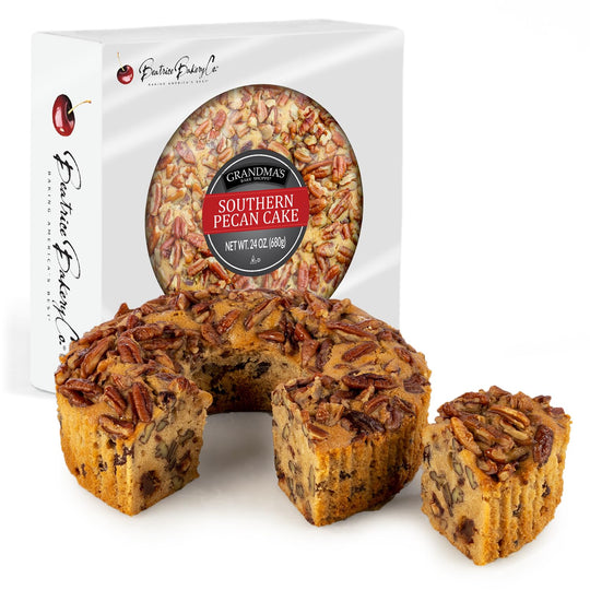 A photo of Southern Pecan Cake by Beatrice Bakery, showing the cake inside a transparent round box with pieces cut out to reveal the pecan toppings.