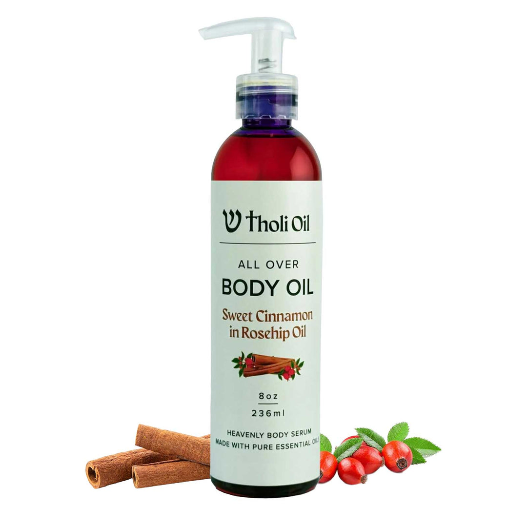 Bottle of Tholi Oil All Over Body Oil with cinnamon sticks and rosehips on a white background
