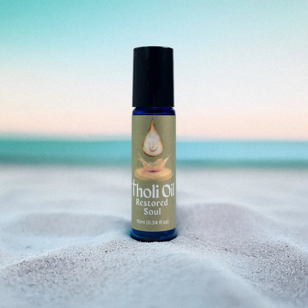 Bottle of 'tholi Oil Restored Soul' on a sandy beach with a blurred ocean background