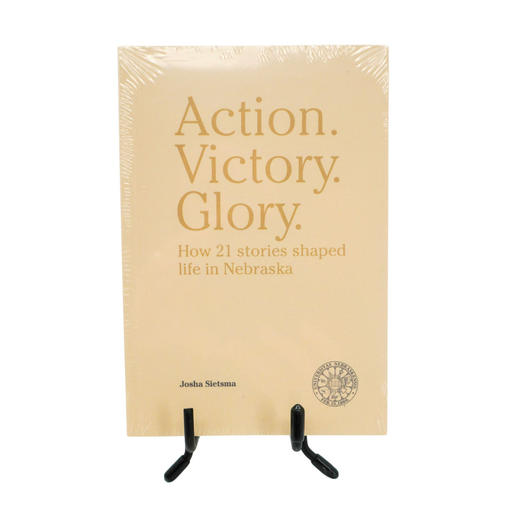 Book titled 'Action. Victory. Glory.' on a stand with beige cover and gold text.
