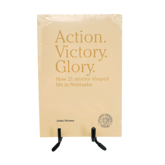 Book titled 'Action. Victory. Glory.' on a stand with beige cover and gold text.