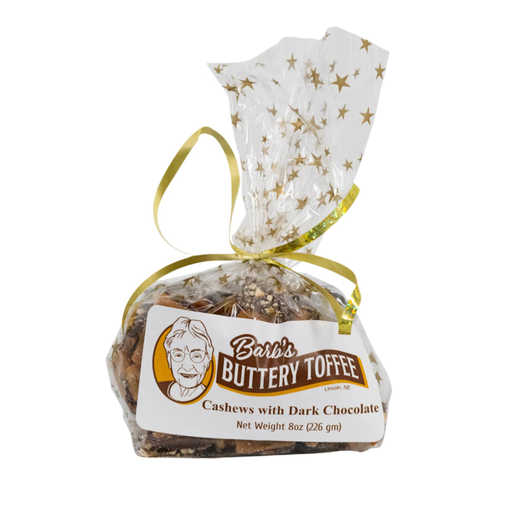 A packaged product of Barb's Buttery Toffee, featuring homemade dark chocolate toffee with cashews, tied with a gold ribbon on a white background.