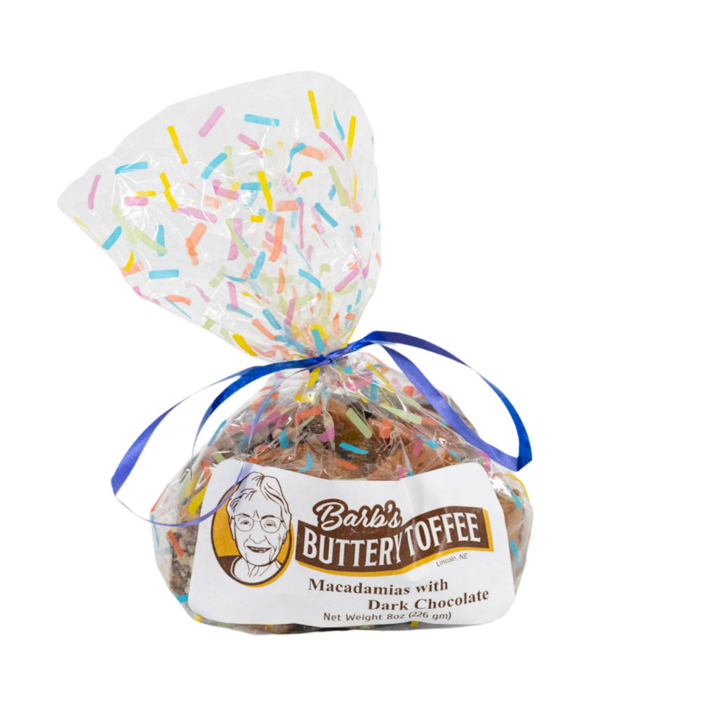 A packaged product of Barb's Buttery Toffee, featuring homemade dark chocolate toffee with macadamia nuts tied with a blue ribbon on a white background.