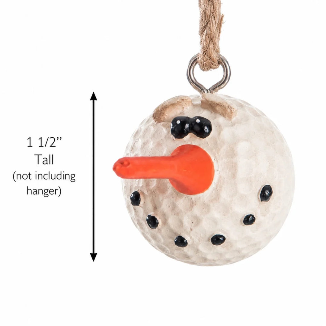 A snowman ornament made from a textured white golf ball with a bright orange carrot nose, black dot eyes and hands, and a brown twig-style hat, hanging from a rope hanger. A vertical measurement arrow on the left indicates the height is 1 1/2 inches tall (not including the hanger).