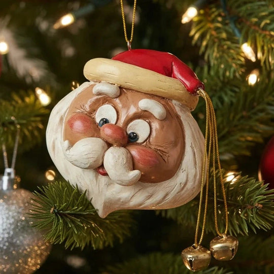 A festive Santa Claus Christmas ornament hanging on a decorated Christmas tree. The ornament features a detailed Santa face with a red hat, gold trim, white beard, and rosy cheeks, with small gold bells dangling from the side.