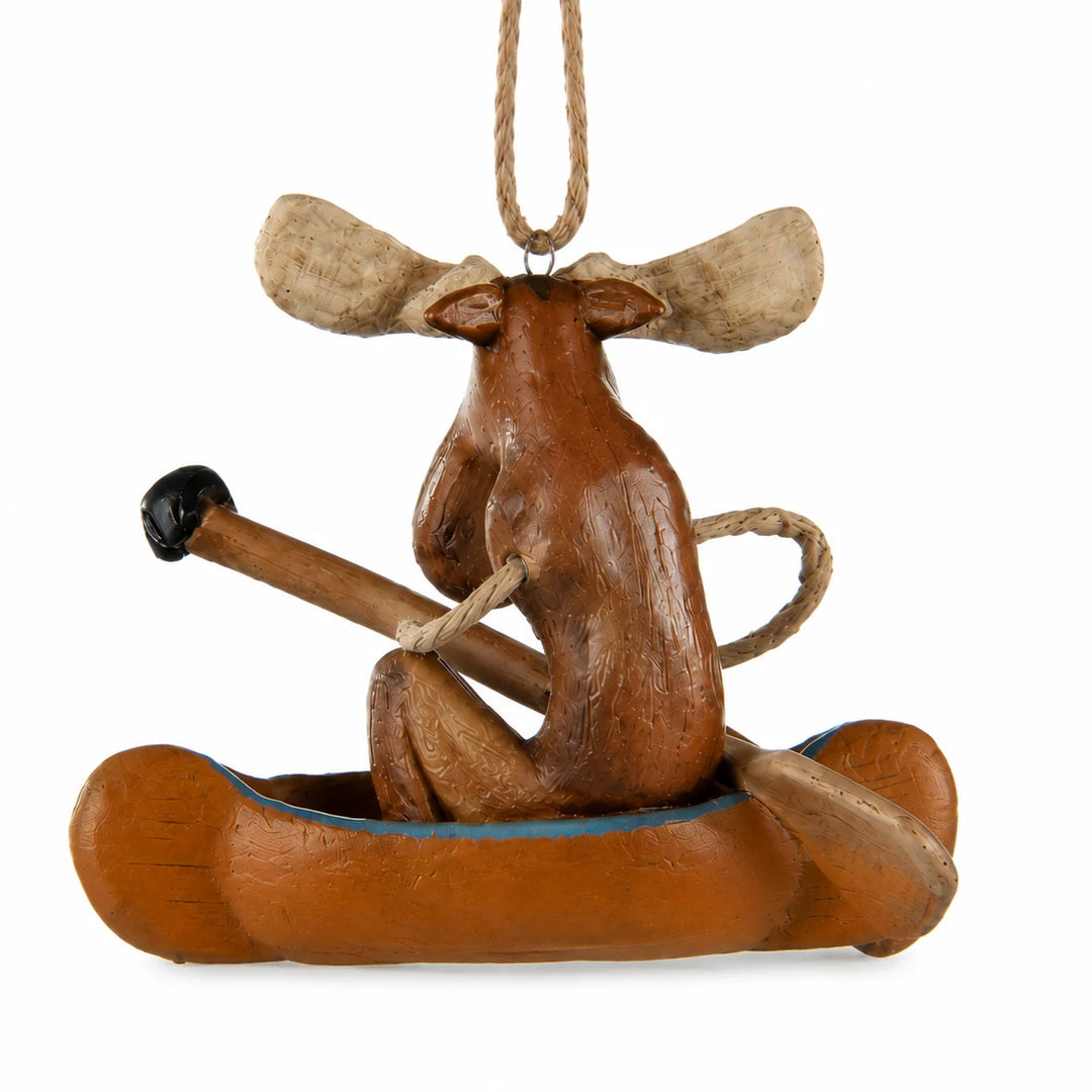 A carved wooden moose ornament sitting in a canoe and holding a paddle, hanging by a rope on a white background.