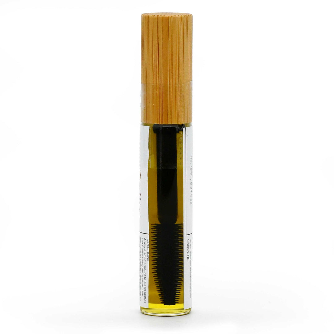 A clear cylindrical cosmetic tube containing a dark brown hair product, topped with a light natural bamboo cap, shown on a plain white background.