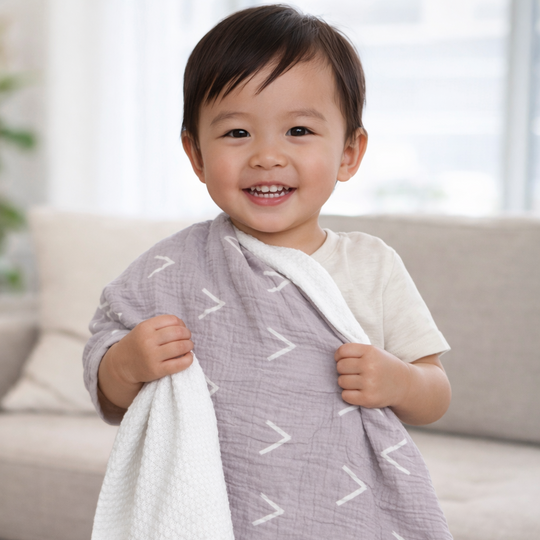 Child holding a gray and white patterned blanket in a living room setting