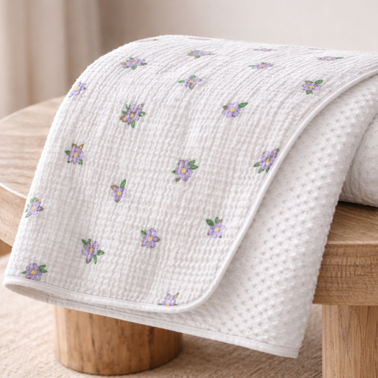Folded white blanket with floral patterns on a wooden surface