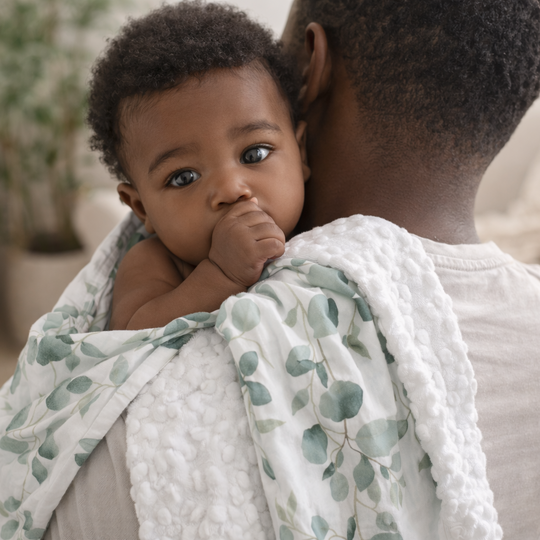 Baby wrapped in a green and white blanket held by an adult in a home setting.