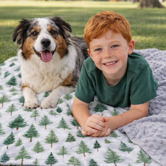 Child and dog lying on a blanket with a forest pattern in a grassy area