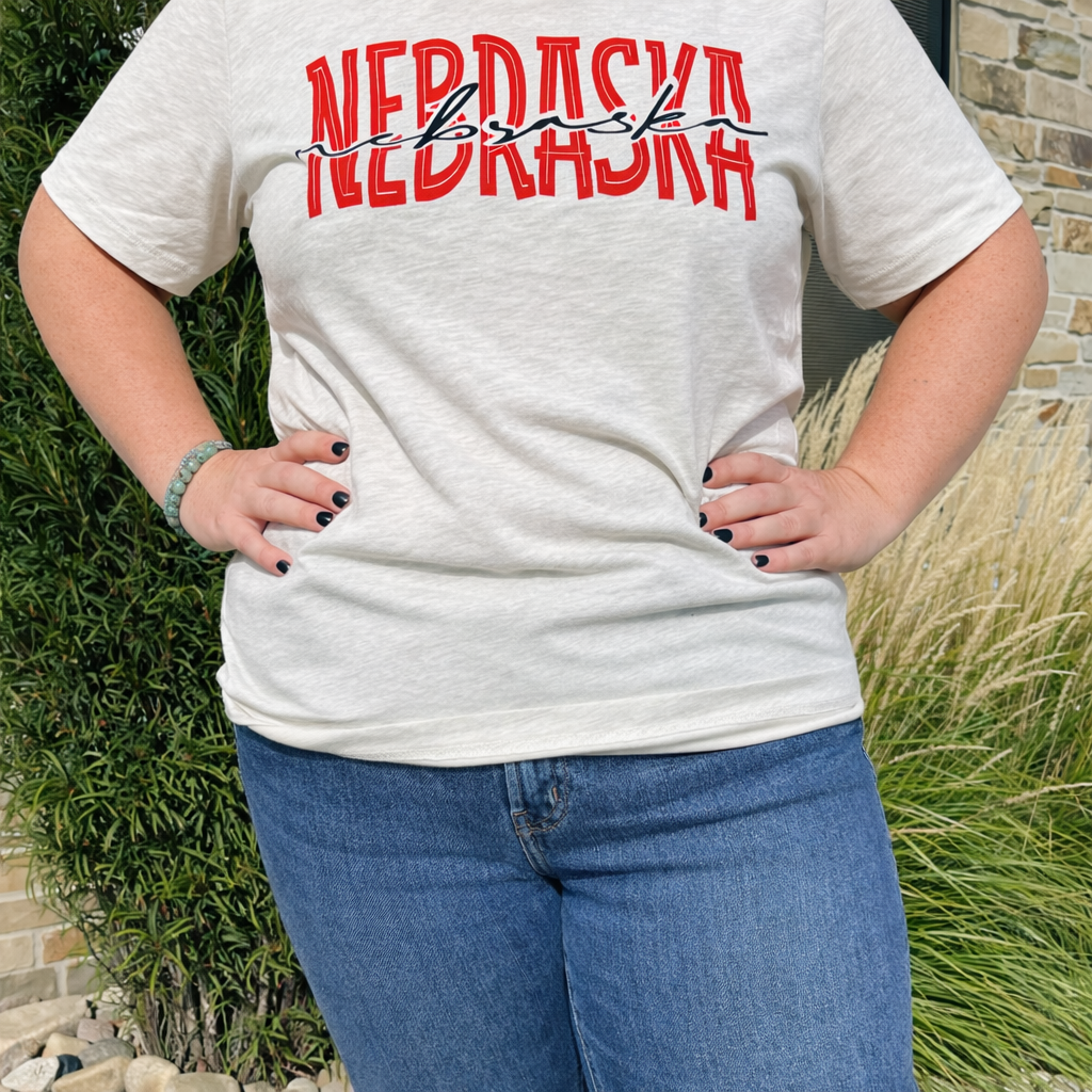 Person wearing a white t-shirt with 'NEBRASKA' printed in red and black, standing outdoors.