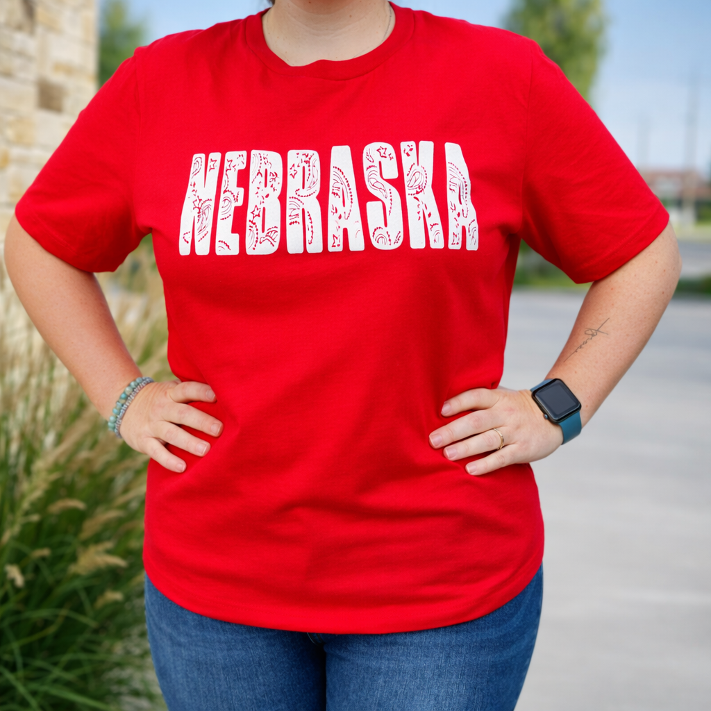 Person wearing a red t-shirt with 'NEBRASKA' printed on it, standing outdoors.