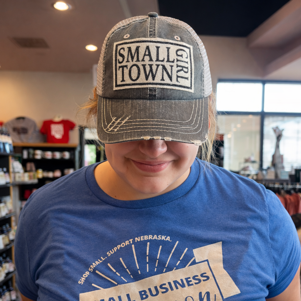 Person wearing a cap with 'Small Town Girl' text in a store setting