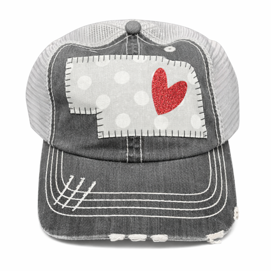 Gray trucker cap with a red heart and white polka dot patch on a white background