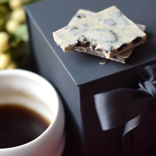 Cookies and cream chocolate bar on a black box with a cup of coffee in the foreground